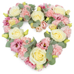 A soft, romantic heart-shaped floral tribute dominates the image, set crisply against a clean white background so that every petal and leaf stands out. The heart is densely packed with blooms, creating a luxurious, cushion-like effect that looks both comforting and elegant. Cream and pale yellow roses serve as the main focal flowers; their velvety petals spiral tightly from the centre into rounded, full blooms that catch the light with a subtle, satin sheen. Between these roses, clusters of pastel pink carnations form a delicate tapestry of ruffled texture, their softly frayed edges giving the wreath a gentle, almost vintage charm. Weaving through the design are deeper magenta-pink lisianthus blossoms, some more open and relaxed, their smooth, layered petals adding a graceful fluidity. Silvery-green eucalyptus leaves thread throughout, their cool tones and rounded shapes outlining the heart and lending a tranquil, airy contrast to the warm florals. Tiny buds in yellow-green scatter lightly through the foliage, suggesting freshness and a life recently in bloom. The overall palette of creams, blush pinks, and muted greens conveys peace, love, and quiet remembrance. It feels like a piece created for a reflective moment, perhaps placed at a funeral service or graveside in Nunhead Cemetery, or delivered to a family home near Brockley and Peckham Rye as a symbol of shared grief. Crafted in the manner of Flower Delivery Nunhead's local artisans, this heart wreath offers a compassionate visual expression when offering condolences and honouring cherished memories in the Nunhead community.